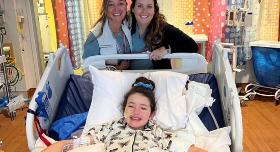 Photograph of a young girl named Collyns in lying in a hospital bed posing with friends.