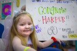 Photograph of a young girl named Harper smiling in front of a white board that says