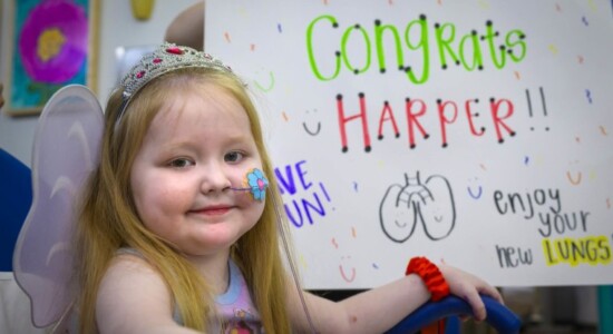 Photograph of a young girl named Harper smiling in front of a white board that says 