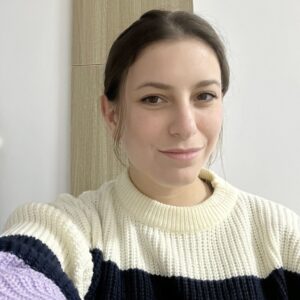Photo of a young woman with dark hair in a cream and navy sweater indoors