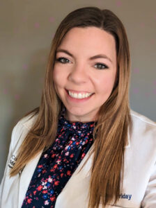 Headshot of a smiling woman in a white lab coat over a floral blouse.