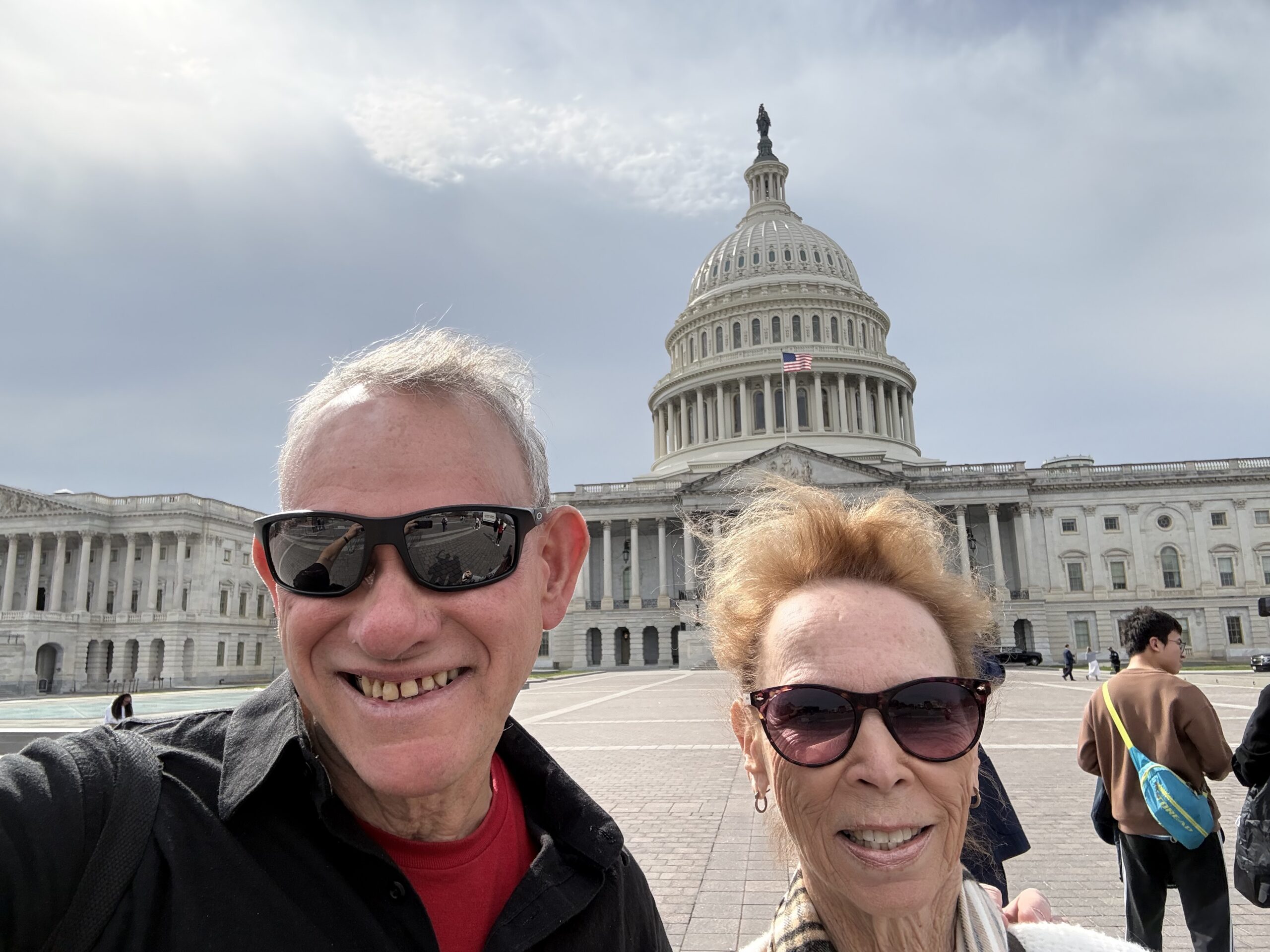 Two people in sunglasses take a selfie in front of the US Capitol dome