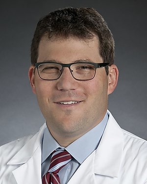 Headshot of a man in glasses wearing a white coat and a red striped tie.