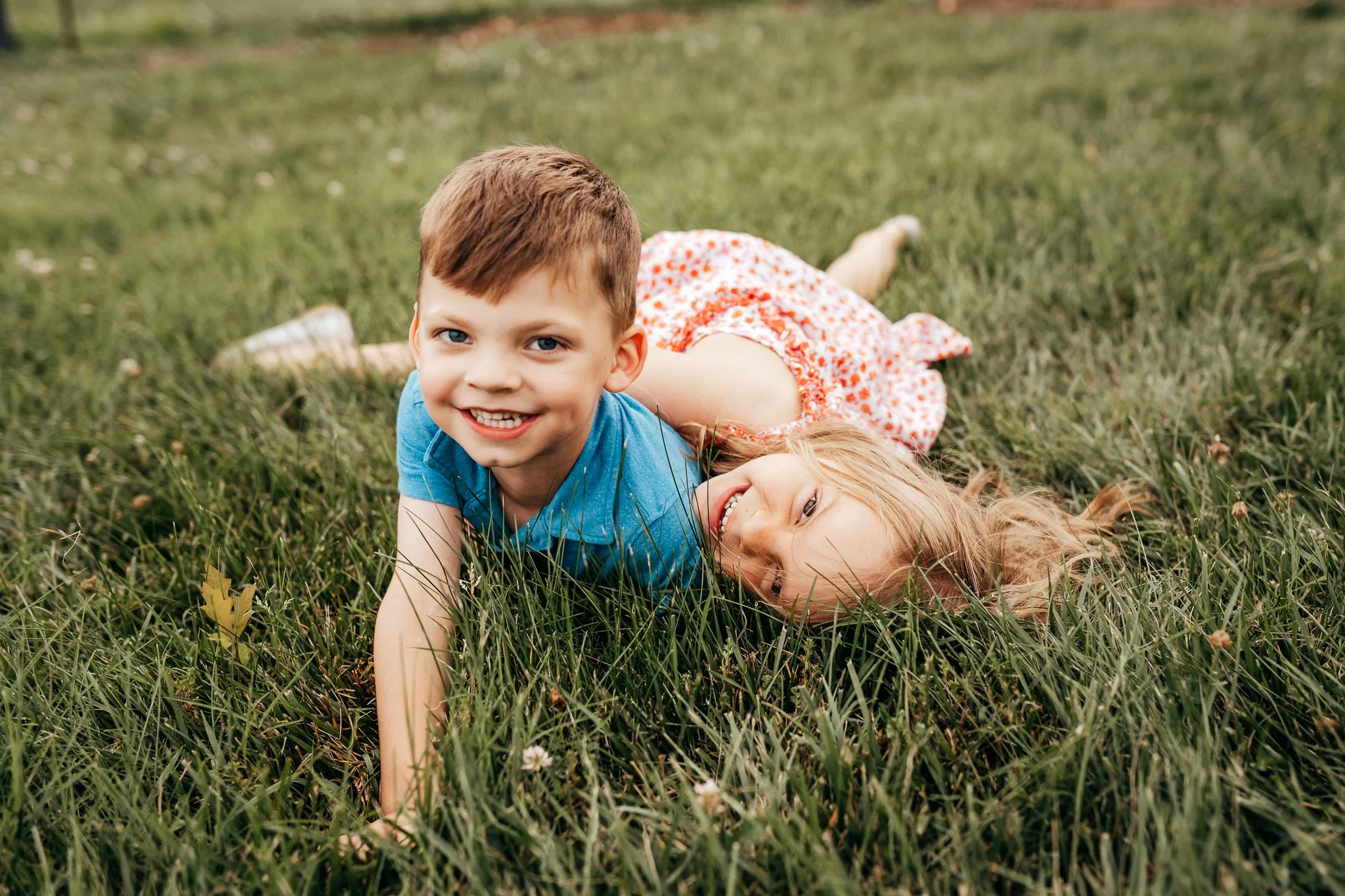 Two young children lying on grass outdoors, smiling at the camera