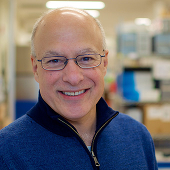 Headshot of a smiling man in glasses and a blue quarter-zip standing in a lab.