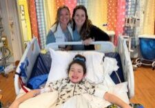 Photograph of a young girl named Collyns in lying in a hospital bed posing with friends.