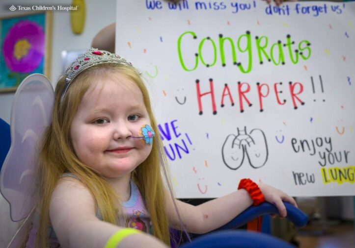 Photograph of a young girl named Harper smiling in front of a white board that says "Congrats Harper" with a drawing of lungs